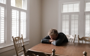 Man sitting at table with his head in his hands.