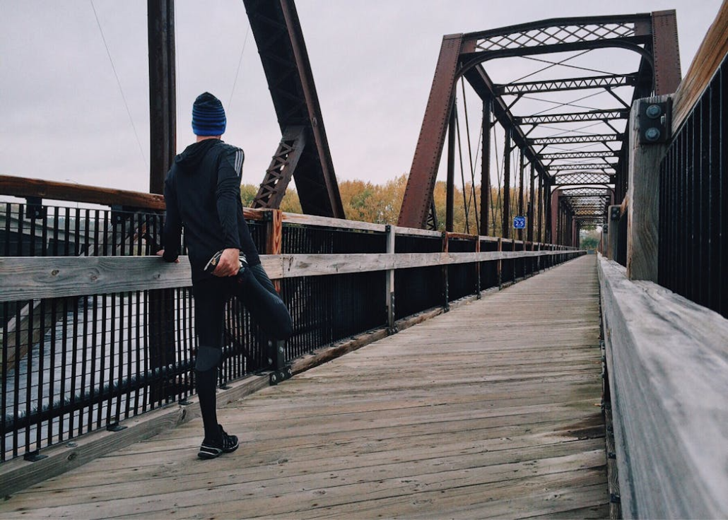 An image of a man stretching his legs on a bridge
