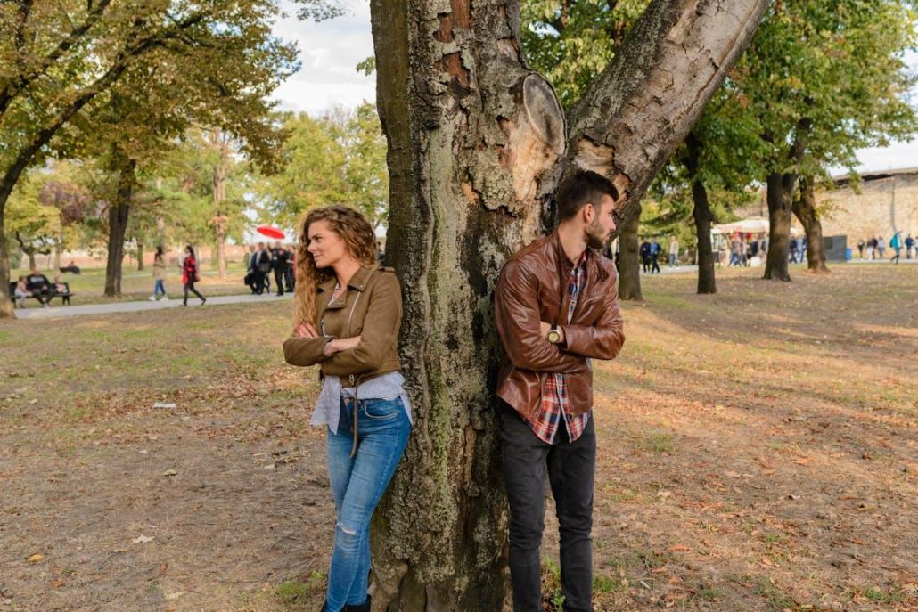 Man and woman wearing leather jackets standing under a tree.