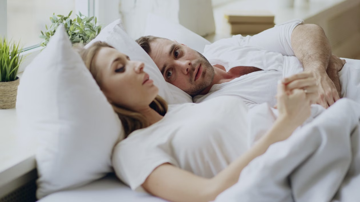 Couple lying in bed appearing emotionally distant while facing relationship strain related to compulsive sexual behavior